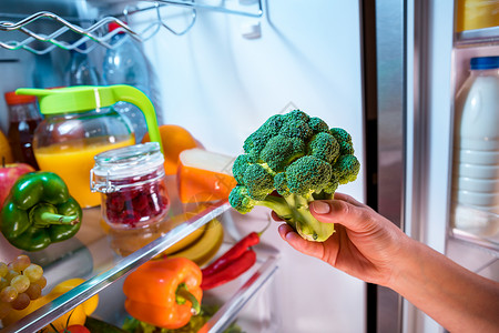 女人打开的冰箱里花椰菜健康的食物图片