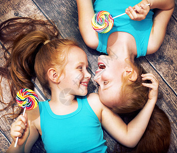 双胞胎姐妹着五颜六色的棒棒糖的美丽肖像高清图片