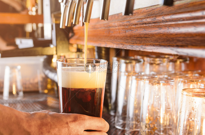 酒保用手酒吧的水龙头把生啤酒倒璃上酒吧男招待正水龙头供应啤酒图片