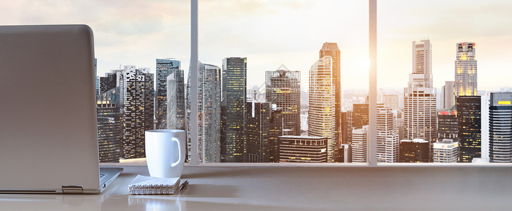 全景的工作场所笔记本电脑办公室的桌子上,全景日落视图的现代市中心摩天大楼商业区背景图片