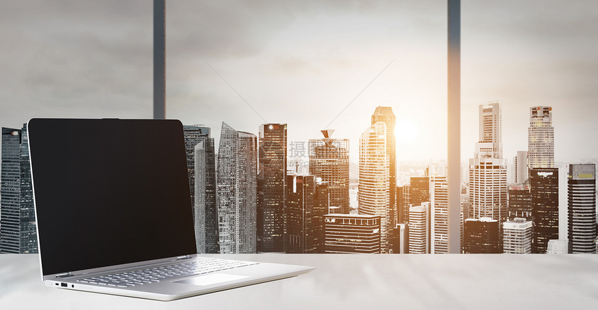 笔记本电脑办公室的桌子上,全景日落的现代市中心摩天大楼商业区,空白屏幕图片