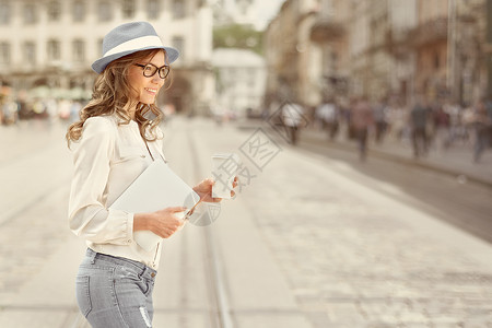 漂亮的轻女人,着次咖啡杯,喝着咖啡,手里着平板电脑,城市背景下过马路图片