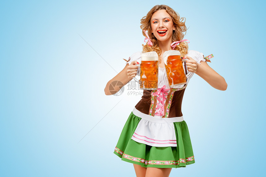 轻感的啤酒节女人穿着件传统的巴伐利亚连衣裙,蓝色背景下为两个啤酒杯提供快乐的微笑图片