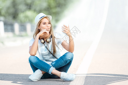 活动分隔导航栏美丽的轻女人,脖子上戴着音乐耳机,智能手机上上网,坐路上的条分隔条上背景