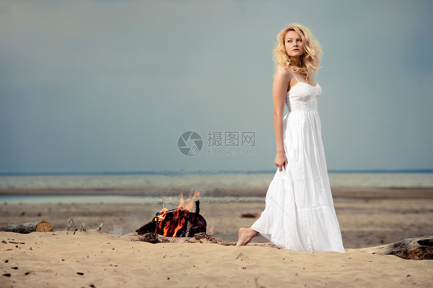 个赤脚的女人穿着白色的衣服海滩上,靠近明火图片