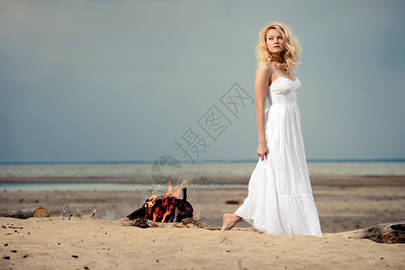 个赤脚的女人穿着白色的衣服海滩上,靠近明火背景图片