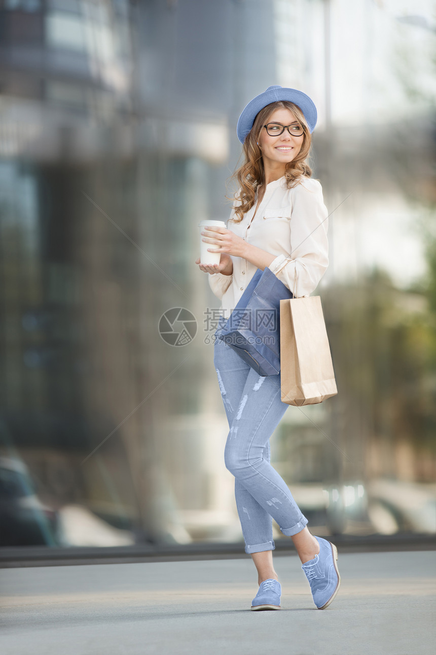 快乐的轻时尚女喝着咖啡,着购物袋站楼梯上,微笑着城市背景图片