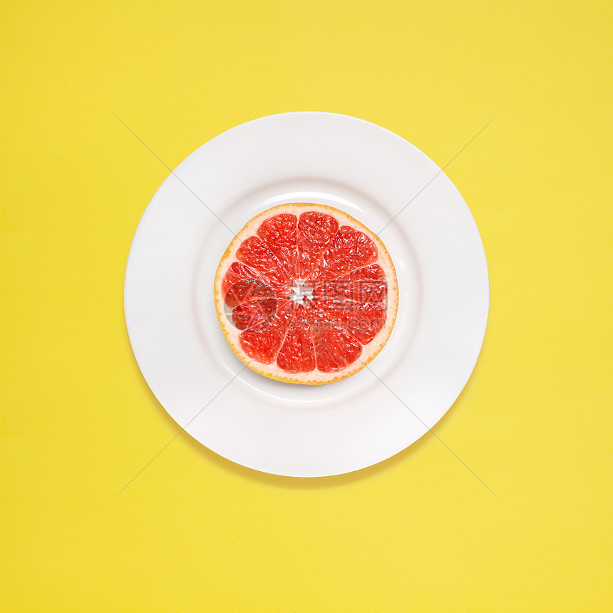 黄色背景上白色盘子上的红色葡萄柚切片图片