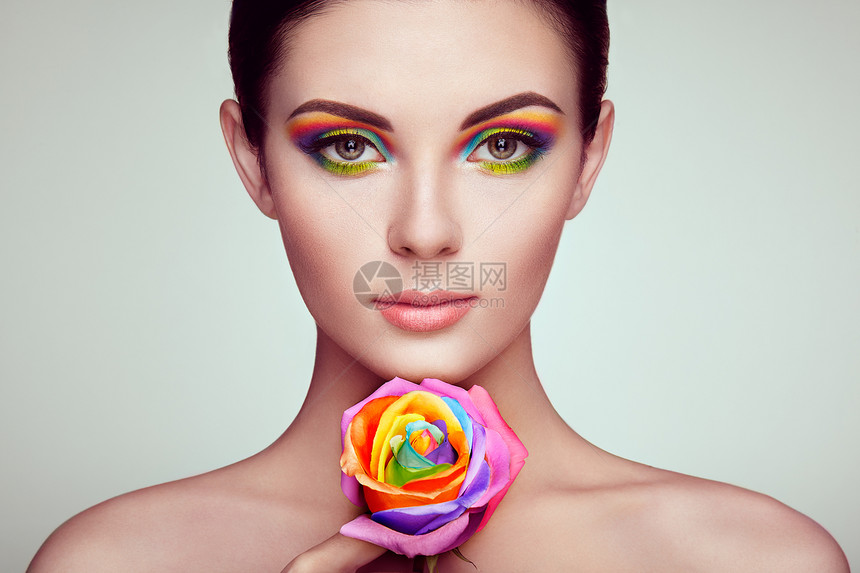 美丽的轻女子与彩虹玫瑰的肖像明亮的颜色长长的睫毛,生动的五颜六色的眼影彩虹化妆五颜六色的花图片