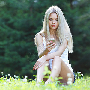 轻的金发女人坐草地上轻的金发女人,着手机坐草地上图片
