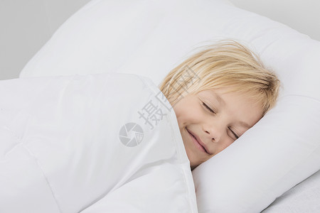 微笑的男孩睡床上开朗微笑的金发男孩睡白色的床上图片
