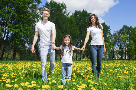 家人公园里走过鲜花快乐的家庭父母女儿走黄色蒲公英花夏季公园背景图片