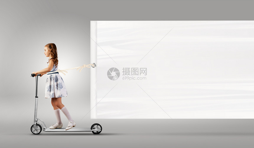 小女孩骑滑板车小女孩骑着滑板车拉着空白的横幅图片
