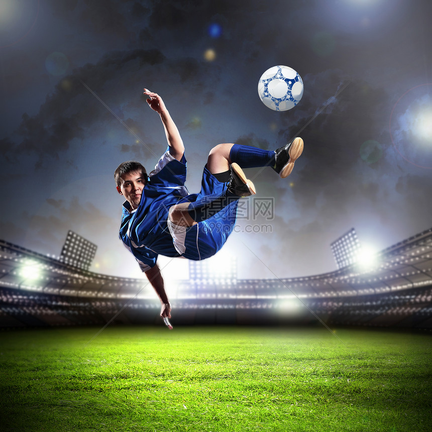 足球运动员击球足球运动员穿着蓝色衬衫体育场把球打得高高的图片