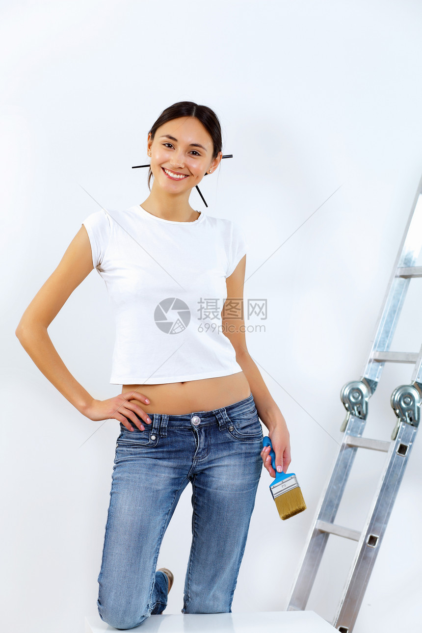 轻的女人用油漆刷翻新白色墙壁图片
