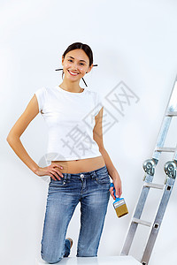 轻的女人用油漆刷翻新白色墙壁背景图片