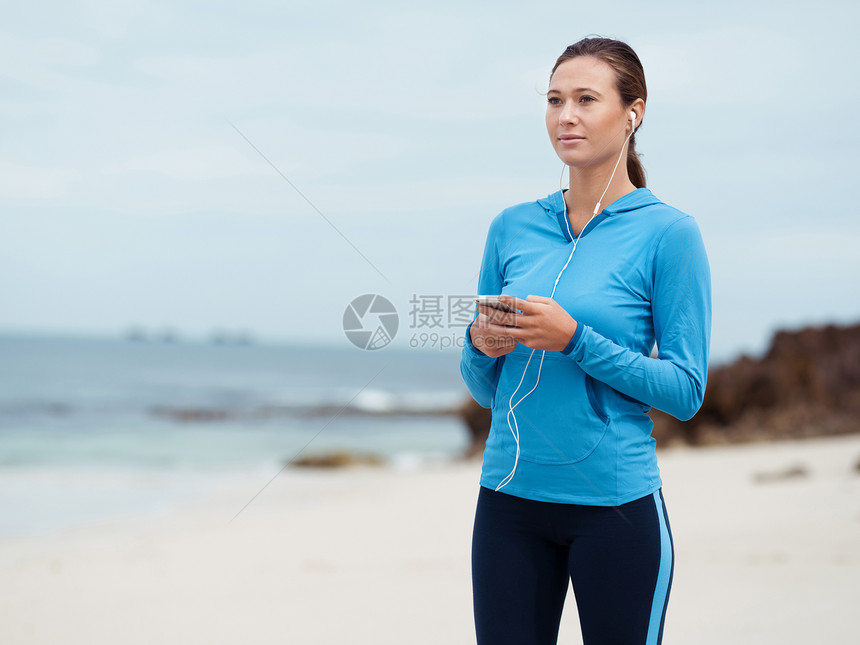海边戴着耳机的运动型轻女人图片