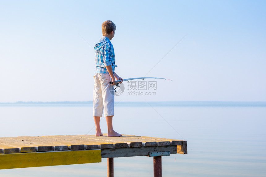 穿着蓝色衬衫的男孩站码头上,海边着鱼竿图片