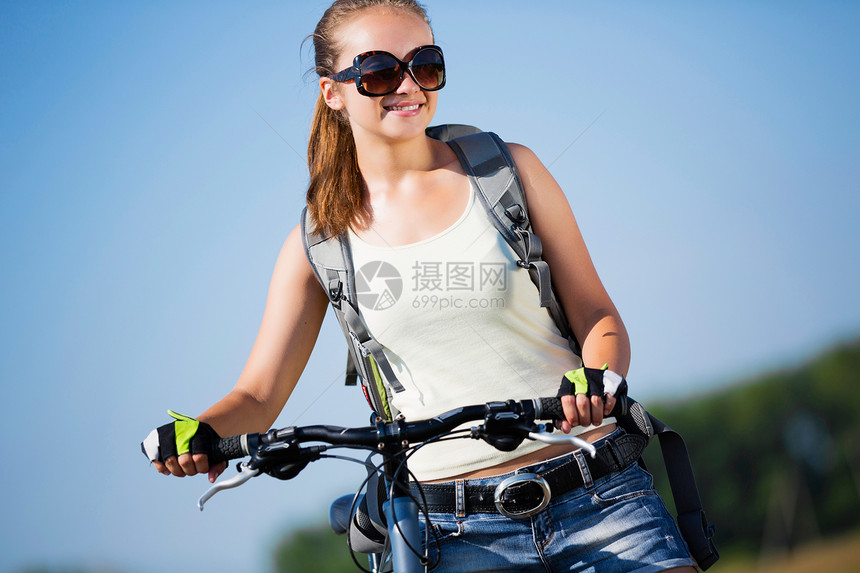 你积极的生活方式轻的运动女孩,背包骑自行车沿路边图片