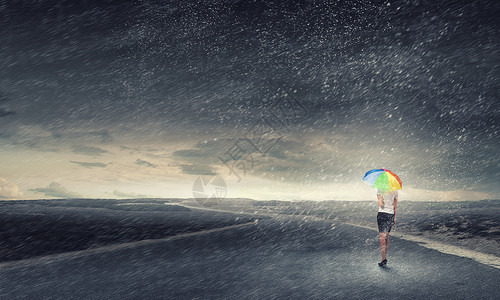 带彩虹伞的女人轻漂亮的女商人带着彩虹五颜六色的雨伞暴风雨中行走背景图片