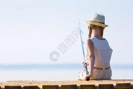 穿着蓑衣钓鱼穿着连衣裙帽子的女孩带着钓鱼竿码头钓鱼背景