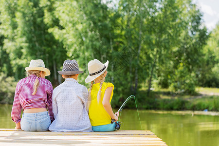 夏季钓鱼池塘夏季休闲三个孩子坐岸边钓鱼的后视镜背景
