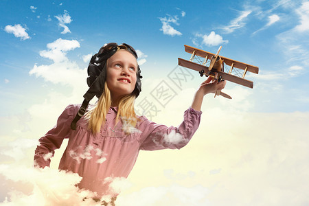 粉色小飞机飞行员头盔中的小女孩云背景下玩玩具飞机的形象背景
