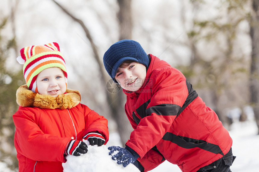 可爱的男孩女孩冬季公园堆雪人冬季活动游戏图片
