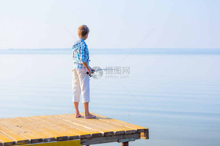 穿着蓝色衬衫的男孩站码头上,海边着鱼竿图片