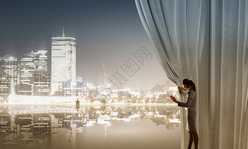女人打开窗帘女商人拉着窗帘城市景观背景图片