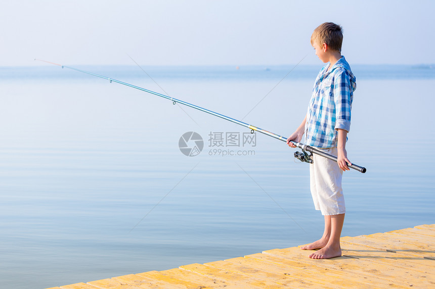 穿着蓝色衬衫的男孩站码头上,海边着鱼竿图片