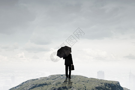 带雨伞的商人站山顶上的商人带着雨伞手提箱的背景高清图片