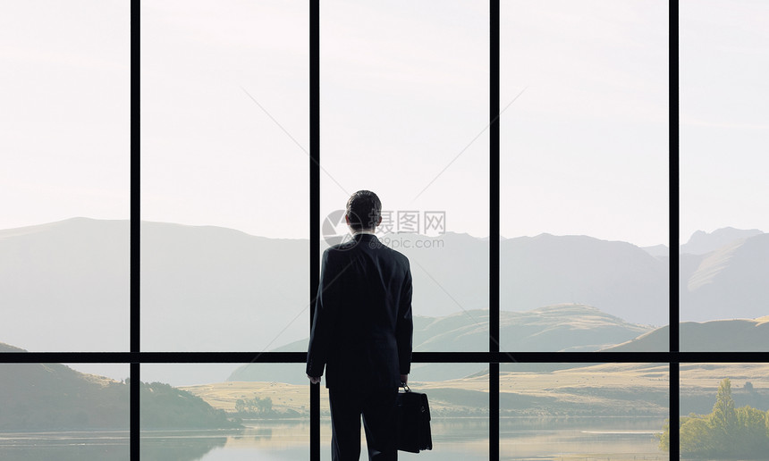 下个成功的日子带着手提箱看办公室窗户的商人的背景图片