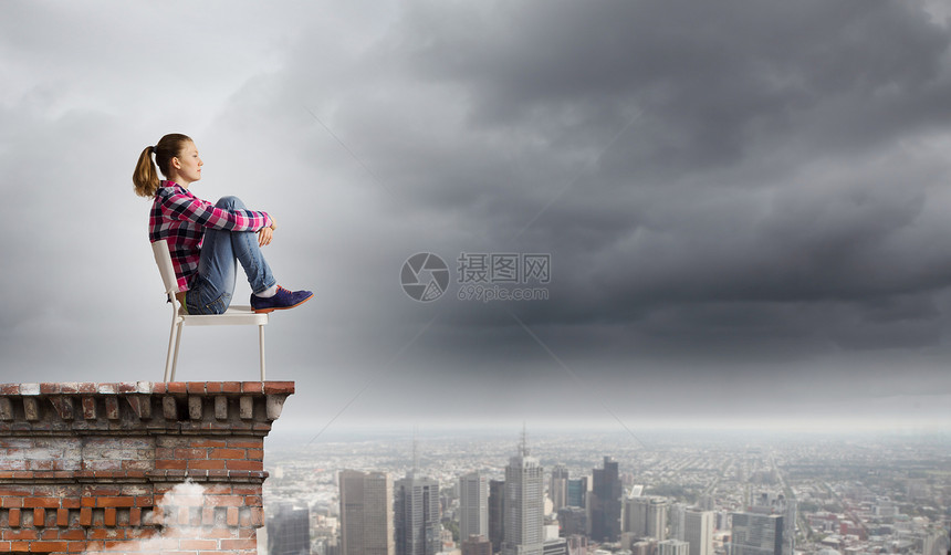 坐椅子上的女人轻的女人随意地坐建筑物顶部的椅子上图片