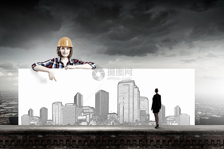 发展项目轻的女建筑工人戴着头盔,着带建筑草图的横幅图片