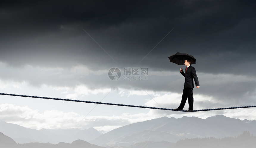 冒险的生意商人用伞平衡绳子上高天空上图片