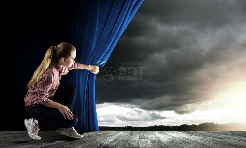 女人窗帘里往外看轻的女人随意地打开蓝色的窗帘,望着天空图片