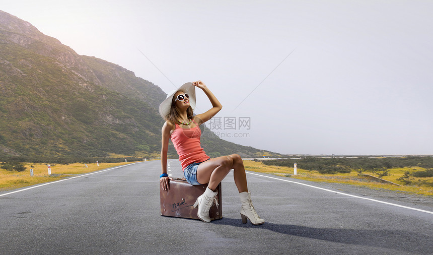漂亮的黑发复古搭便车旅行者女人坐复古手提箱上等车图片