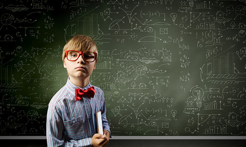 聪明的小学生戴着红色眼镜的天才男孩靠近黑板,公式背景图片