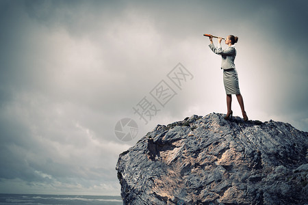 望远镜的商业女人女商人站岩石顶上用望远镜看的形象背景图片