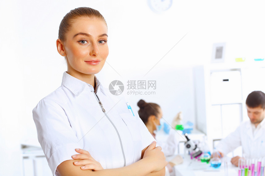 轻的女医生穿着白色制服,背景上同事图片