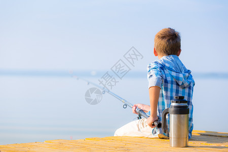 码线穿蓝色衬衫的男孩坐馅饼上穿着蓝色衬衫的男孩坐海边的码头上,着鱼竿背景