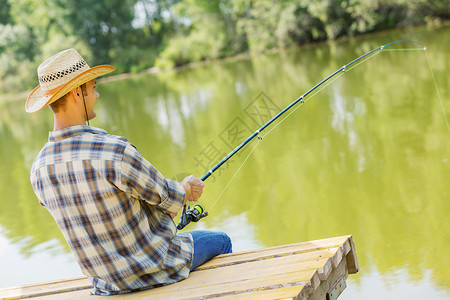 夏天钓鱼戴帽子的轻人坐桥上钓鱼高清图片
