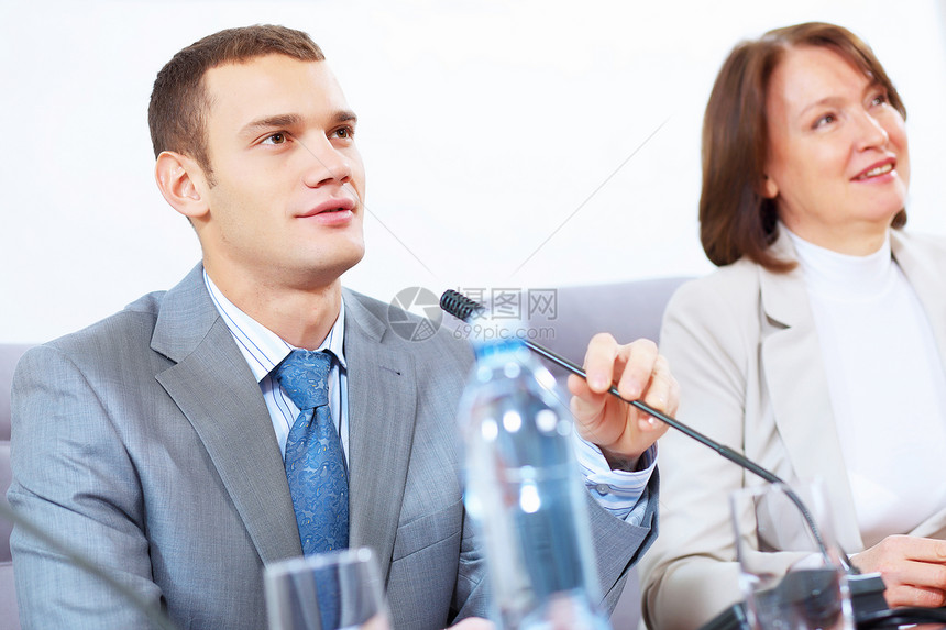两个商人开会两个商人坐桌子上用麦克风说话的形象图片
