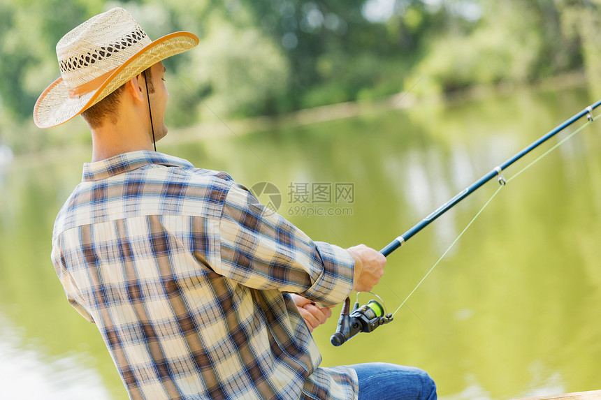 夏天钓鱼戴帽子的年轻人坐桥上钓鱼图片