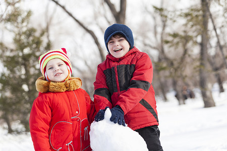 可爱的男孩女孩冬季公园堆雪人冬季活动游戏图片