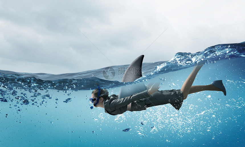 商业世界的鲨鱼带着鲨鱼鳍的轻女商人水下游泳图片