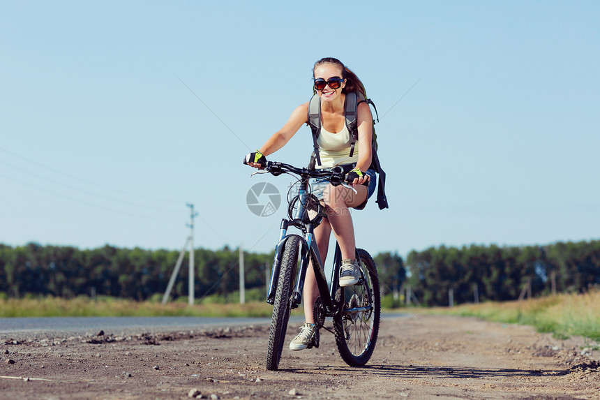 你积极的生活方式轻的运动女孩,背包骑自行车沿路边图片