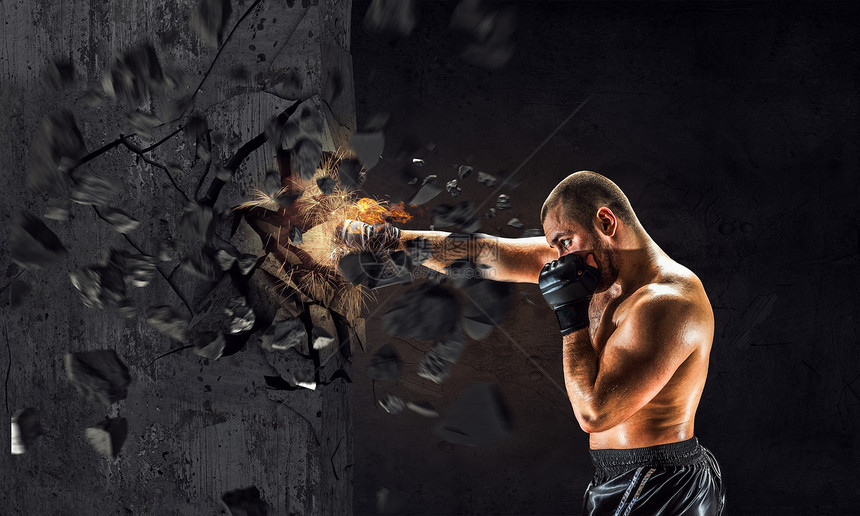 拥力量耐力戴手套打破水泥墙的强壮拳击手图片