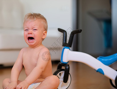 小男孩坐地板上哭背景中的自行车图片
